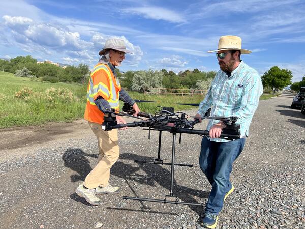 Two pilots carry drone aircraft on gravelly road
