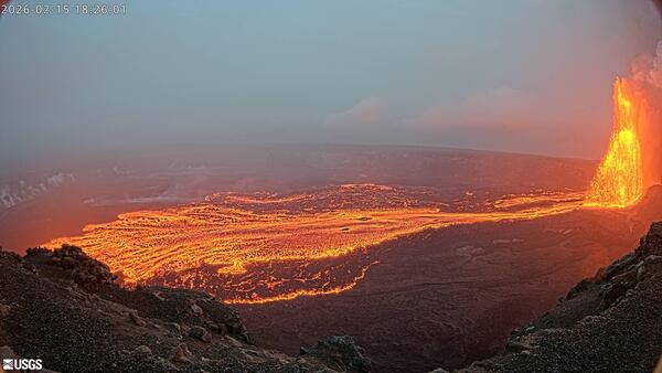 Color photograph of lava fountain feeding lava flows on the floor of a crater