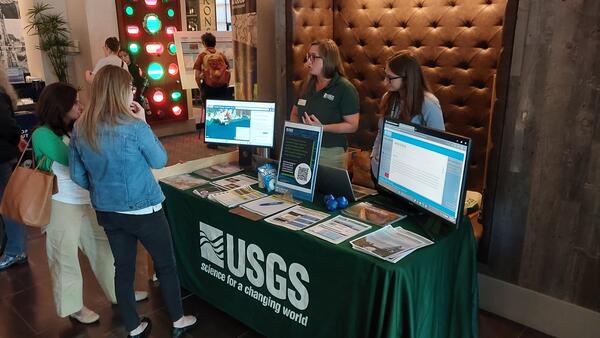 Two USGS scientists behind a booth filled with handouts and computer monitors talking to two visitors