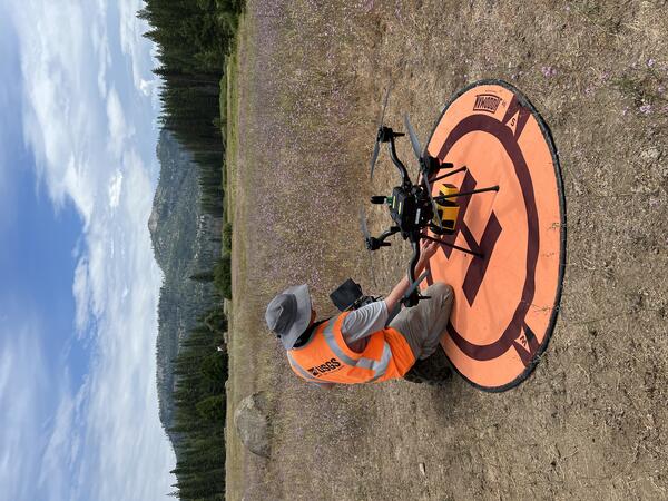 UAS pilot readying craft that sits on landing pad situated in a mountain clearing