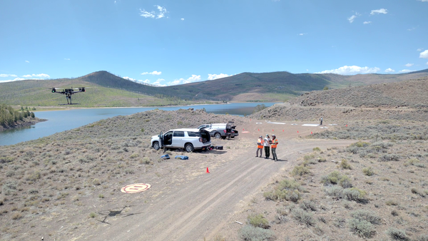 UAS personnel stand next to their vehicles as they control drone above reservoir