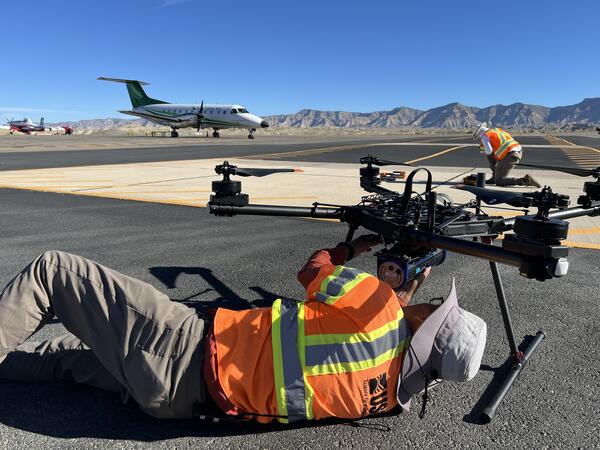 Drone operator laying on airstrip, securing sensors to the underside of UAS craft.