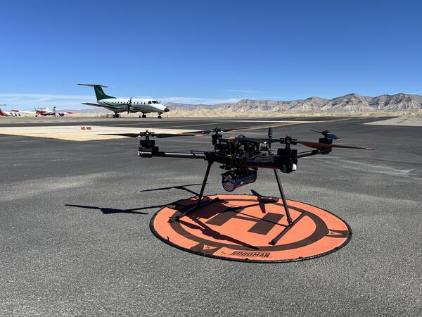 UAS sitting on landing pad at the Grand Junction Regional Airport, with small airplane in background.