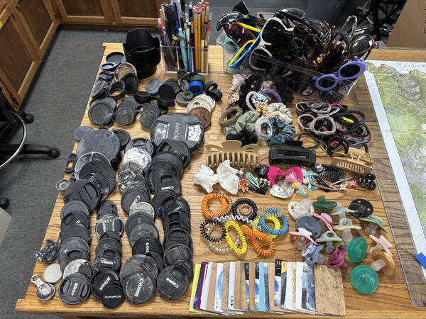 camera lens caps, hair accessories, pacifiers, sunglasses, and hotel key cards laid out on a wooden table