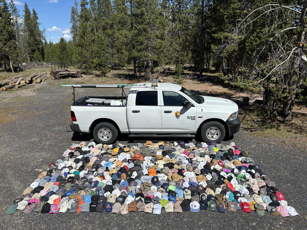 A white pickup truck is parked in front of an array of hundreds of hats of various colors laid out on the ground