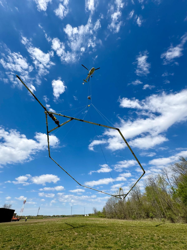 Looking up at a helicopter in flight with scientific instrument under it against a blue sky with white clouds