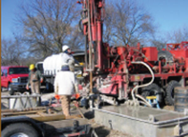 Several people are seen standing near a large underground drilling rig. 