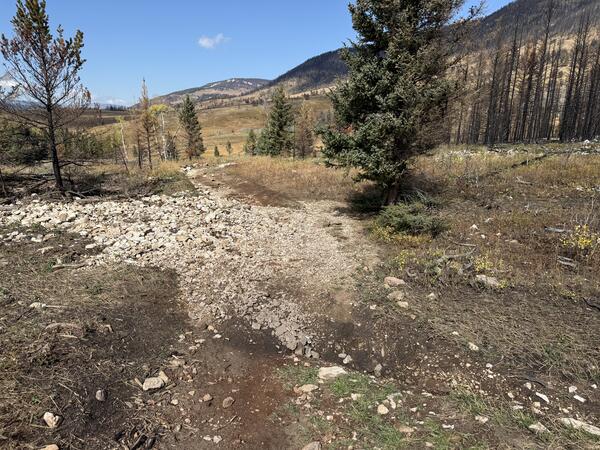 a bile of rocks and mud partially covering a dirt road with mountains visible in the background