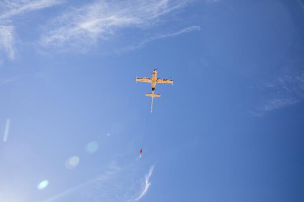 An aircraft glides low, towing instruments to collect data on groundwater and geology.