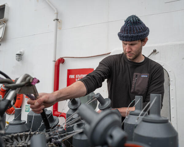 A person in a hat works on Niskin bottles attached to a CTD