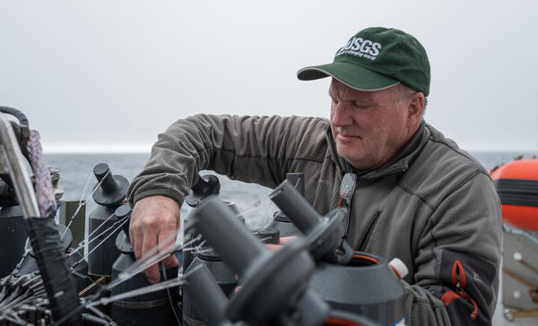 A person in a USGS hat sets Niskin bottles on a CTD