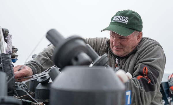 A person in a USGS hat sets Niskin bottles on a CTD
