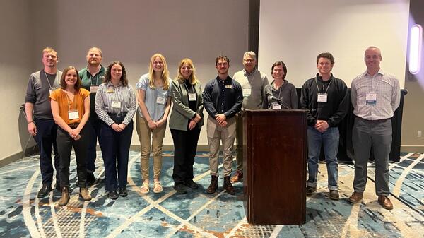 Eleven people at a conference standing in a line smiling for the camera