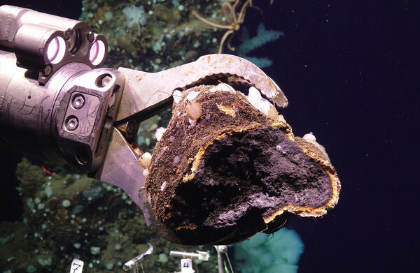 Image of a remotely operated vehicle using a robotic arm to collect a polymetallic sulfide sample from Escanaba Trough
