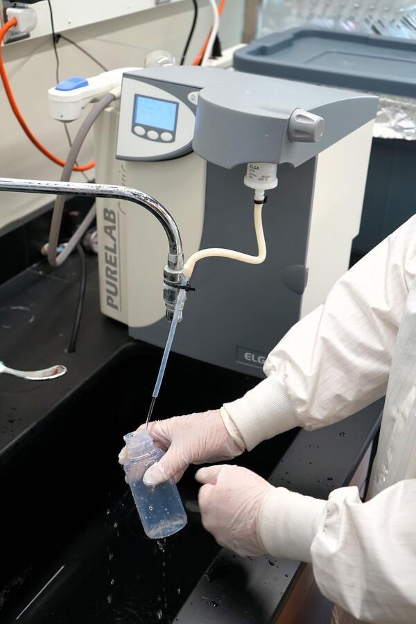 Scientist rinsing white plastic Teflon sample bottle with deionized water in a laboratory