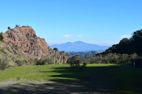 A dark red, rubbly cliff of lava angles sharply into the background over a flat terrace of bright green grass