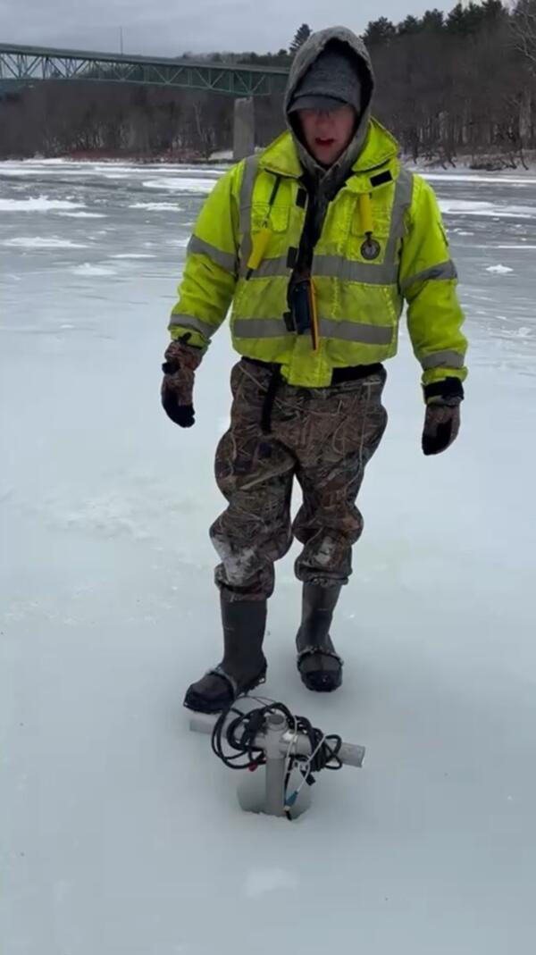 Scientist standing behind borehole in ice with an acoustic probe lowered