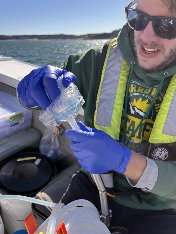 A man in a boat places a filter cap on eDNA equipment during sampling in a reservoir
