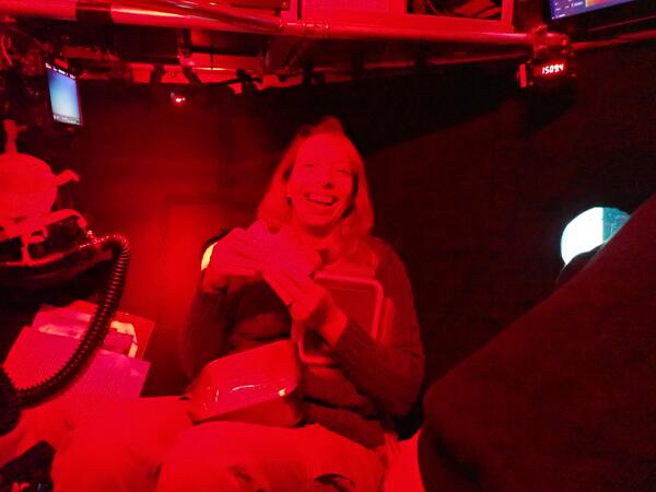 A red light glows over a person smiling and holding a sandwich 