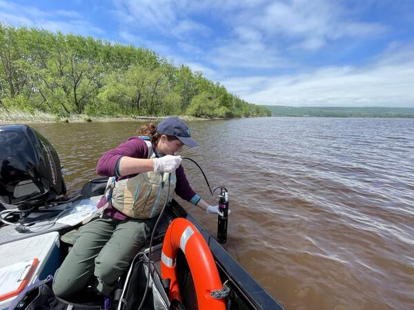 Scientist leans over side of boat to take water quality measurement with a sonde