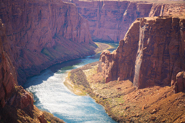 Light reflects off a wide river as it winds through a sheer red-rock canyon.