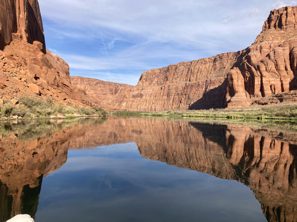 The Colorado River water reflects blue skies and red Grand Canyon walls