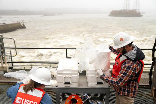 Standing on a catwalk, hydrologic technicians Kelly McVicker and Shane Mizelle prepare to collect water samples from the Conowingo Dam.