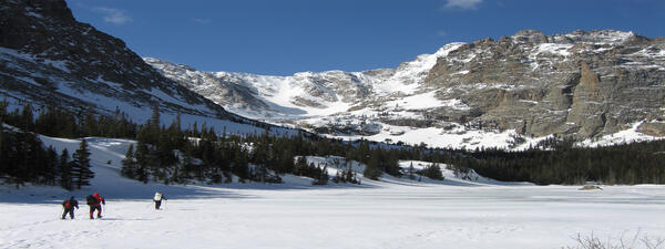 Image of two scientist trekking through snow with Rocky Mountains and trees in background