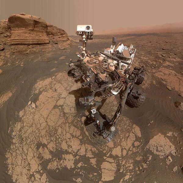 Selfie of MSL Curiosity: a large 6-wheeled rover covered in red dust roving the Mars surface