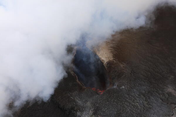 Close-up image of a volcanic vent with red lava surface far below the vent rim