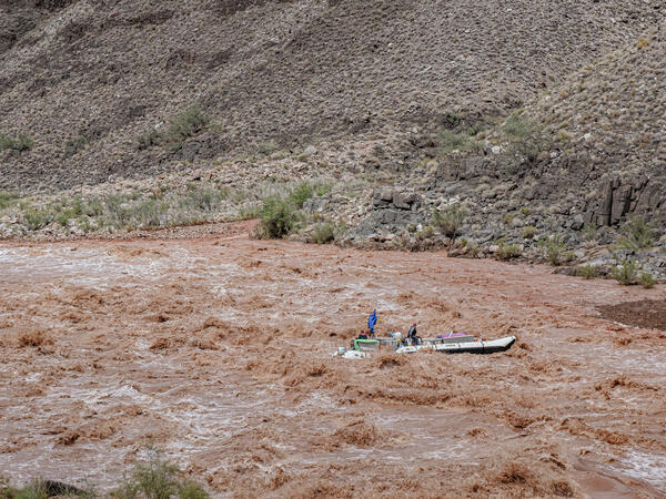 A research boat navigates high rapids in the brown sediment-filled Colorado River during a storm
