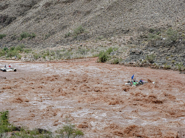 Two boats navigate high rapids in the muddy sediment-filled Colorado River during a rainstorm