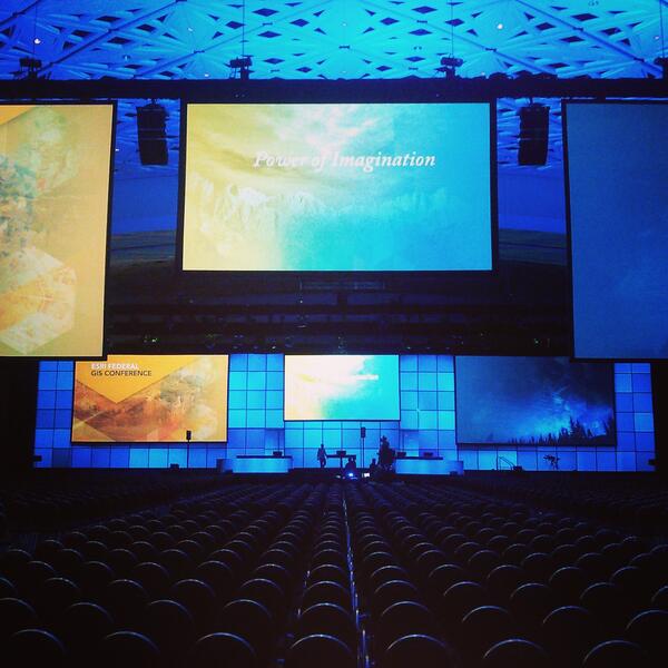 Backlit conference backdrop and stage and a row of seats in the foreground in a low-lit ballroom