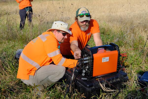 Two scientists wearing orange, look at a mobile WalkTEM unit while in the field.