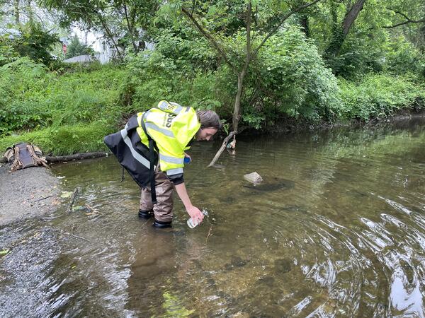 A usgs hydrologic technician collects a water quality sample from a stream