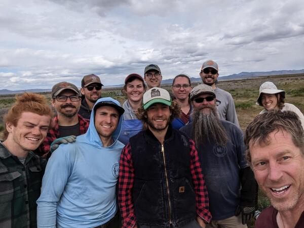 12 folks in the FIREss crew with a sagebrush dominated landscape in the background and clouds in the sky
