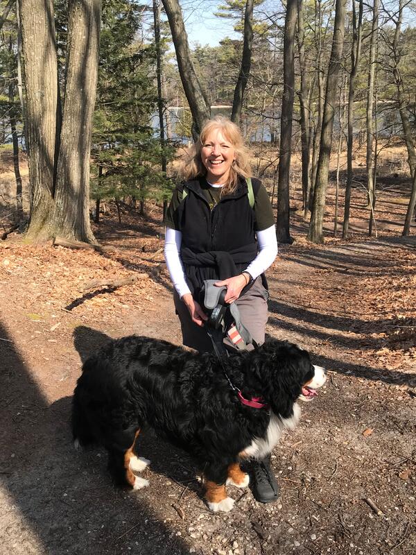 Smiling woman standing with Bernese Mountain Dog on wooded hiking trail