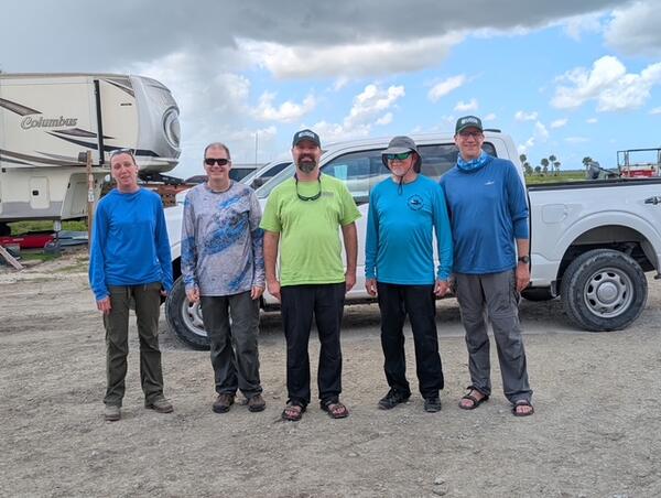 five people stand for a group shot in front of a truck