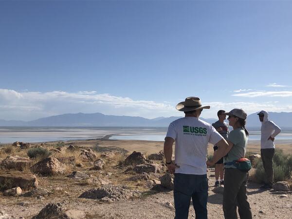 Four scientist looking out over the Great Salt Lake from Antelope Island. There are mountains behind them and clouds 