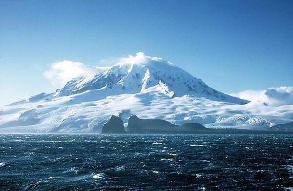 Ice-covered mountain  under blue sky with choppy dark blue ocean water in the foreground