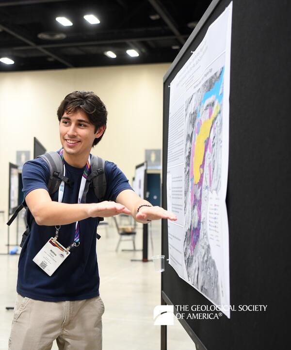 A student stands to the left of their geologic map poster gesturing towards it while presenting the information.