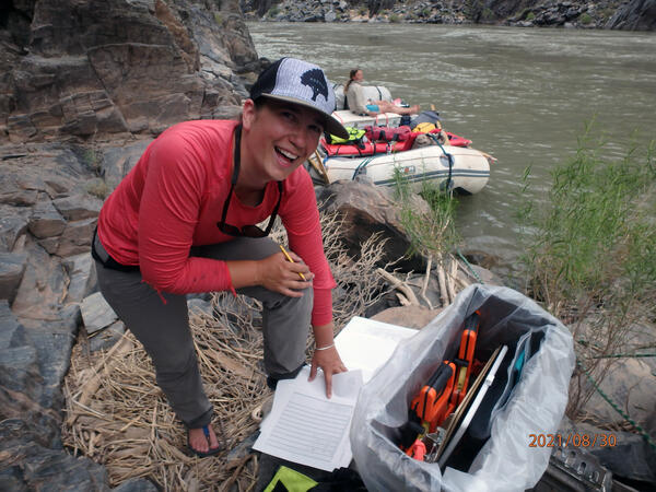 A woman wearing a red long-sleeve shirt laughs during vegetation data collection alongside the Colorado River in Grand Canyon