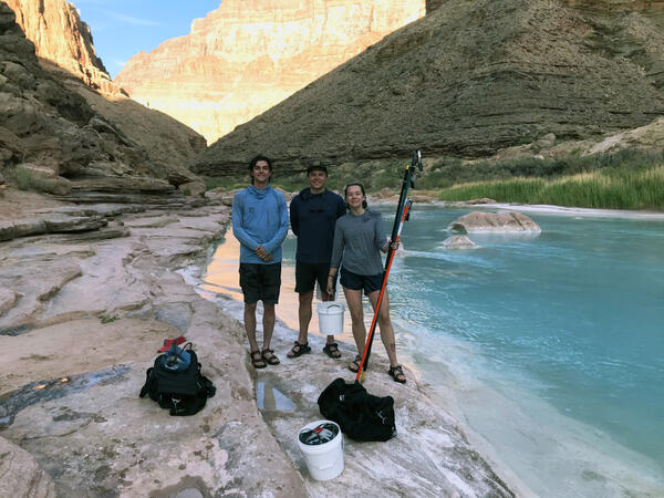 Two young men and a young woman hold eDNA sampling equipment next to the Little Colorado River