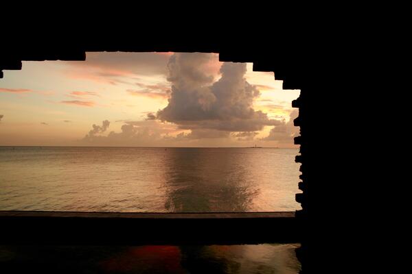 Cloudy sunset over the sea is framed by the jagged window of an historic fort