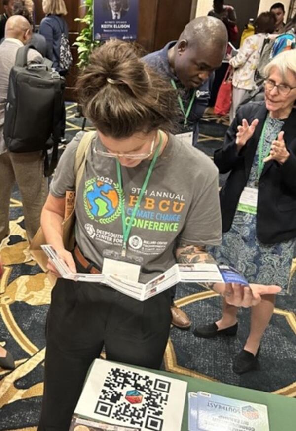 A woman with brown hair wearing a grey shirt and black pants reads an informative card about careers in the USGS. 