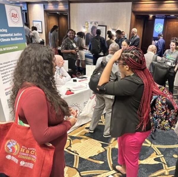 Two women stand next to each other as they look over the conference room of people and informational booths.