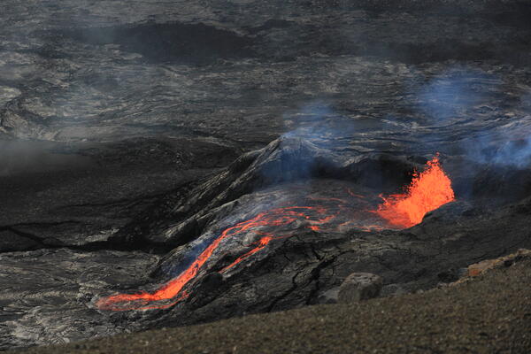 color photo of red hot lava flowing out of the vent, which is all black.