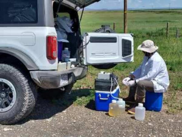 Scientist processing water samples sitting behind a vehicle in front of a field