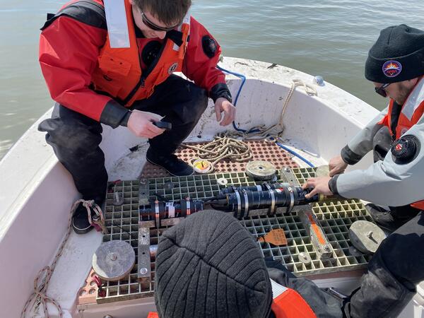 Three people on a small boat working with a small piece of equipment