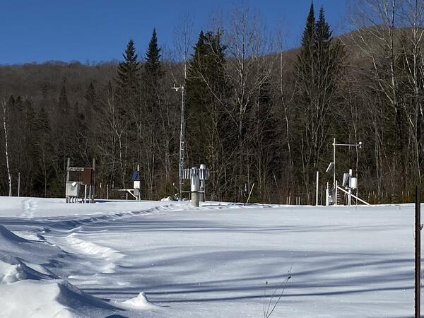Snow monitoring stations in a snowy field with woods in the background.